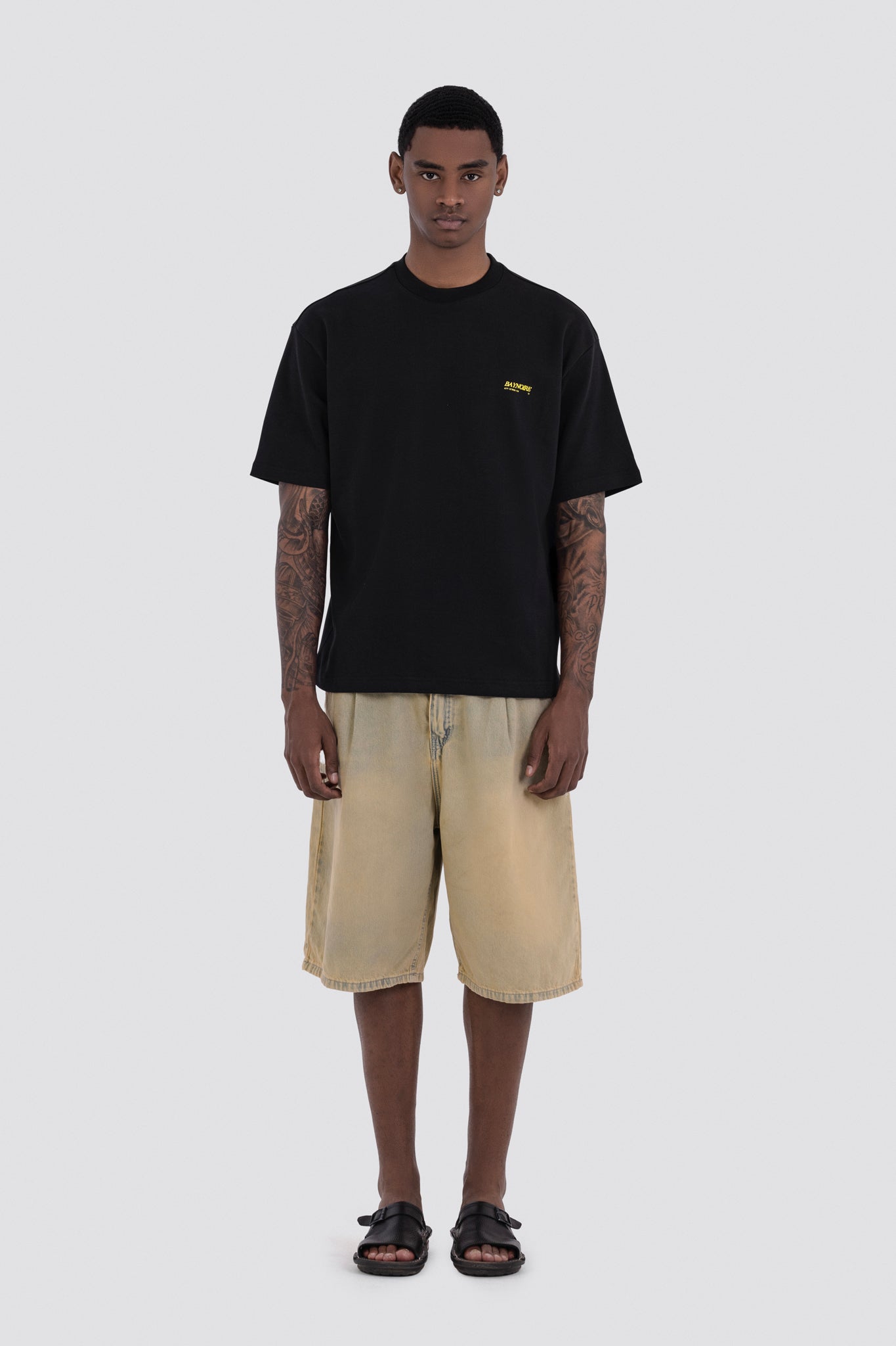 Man wearing a black t-shirt with a logo and beige shorts on a white background