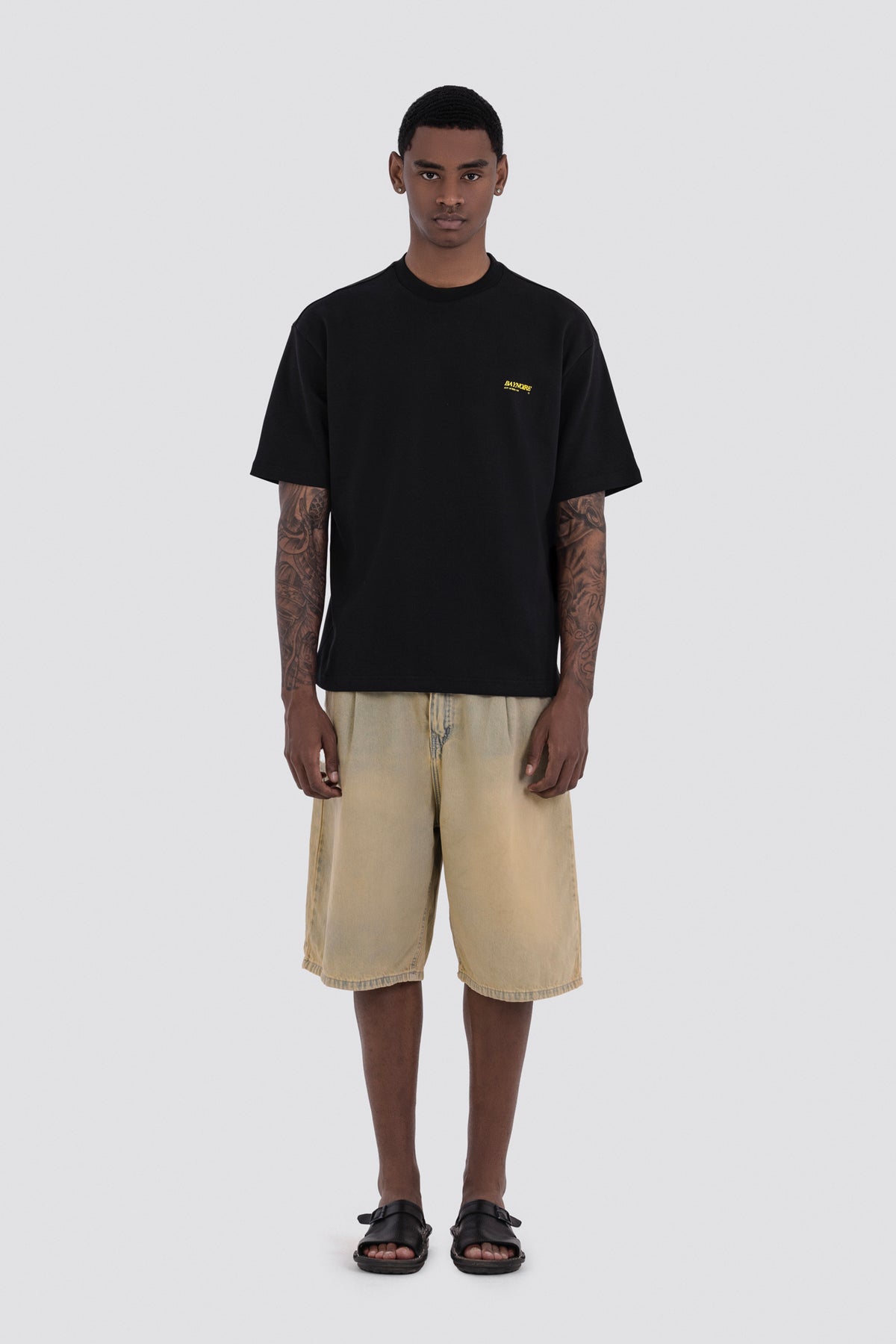 Man wearing a black t-shirt with a logo and beige shorts on a white background