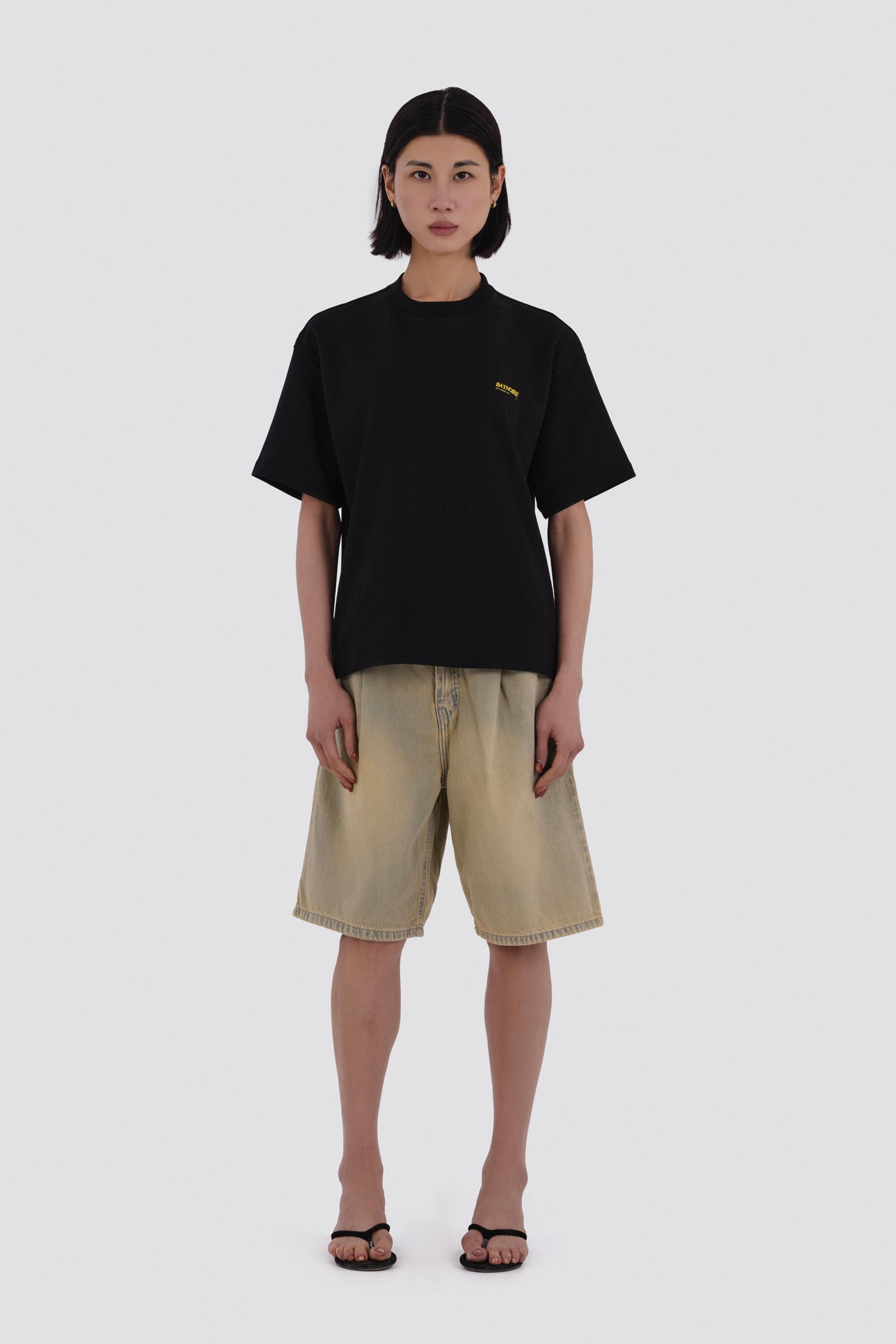 Person wearing a black t-shirt and beige shorts on a white background