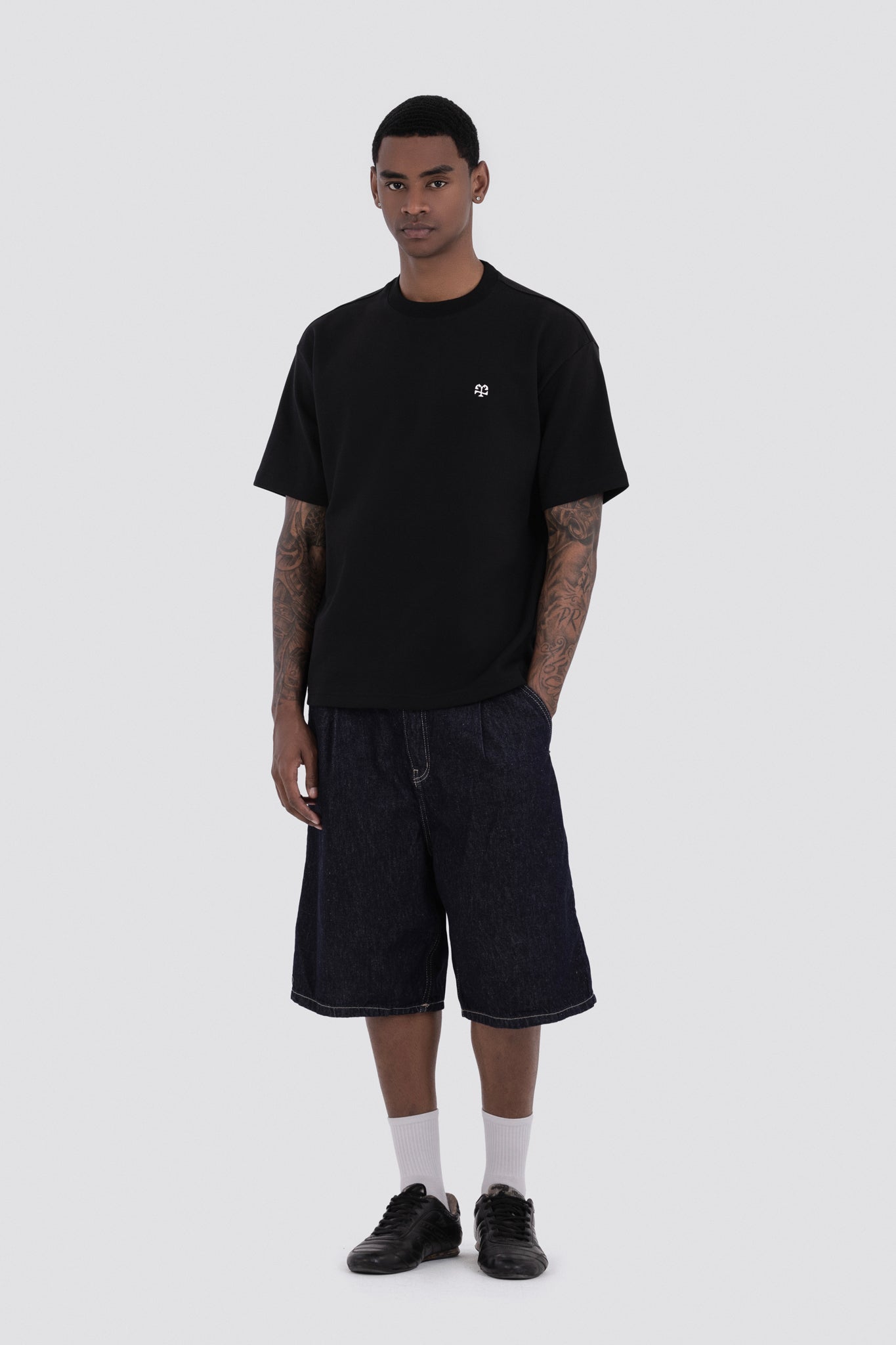 Man wearing a black t-shirt and dark shorts on a white background