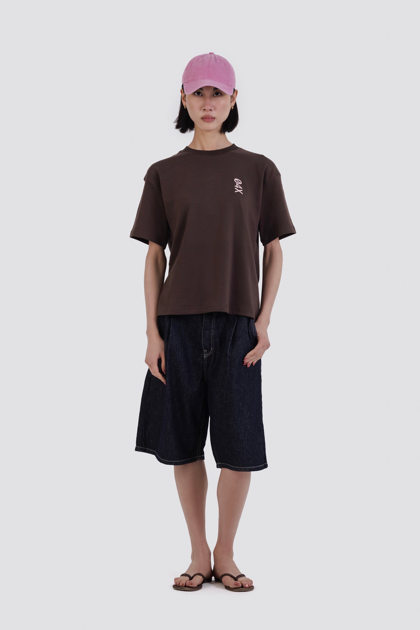Person wearing a brown t-shirt and black shorts with a pink cap on a white background