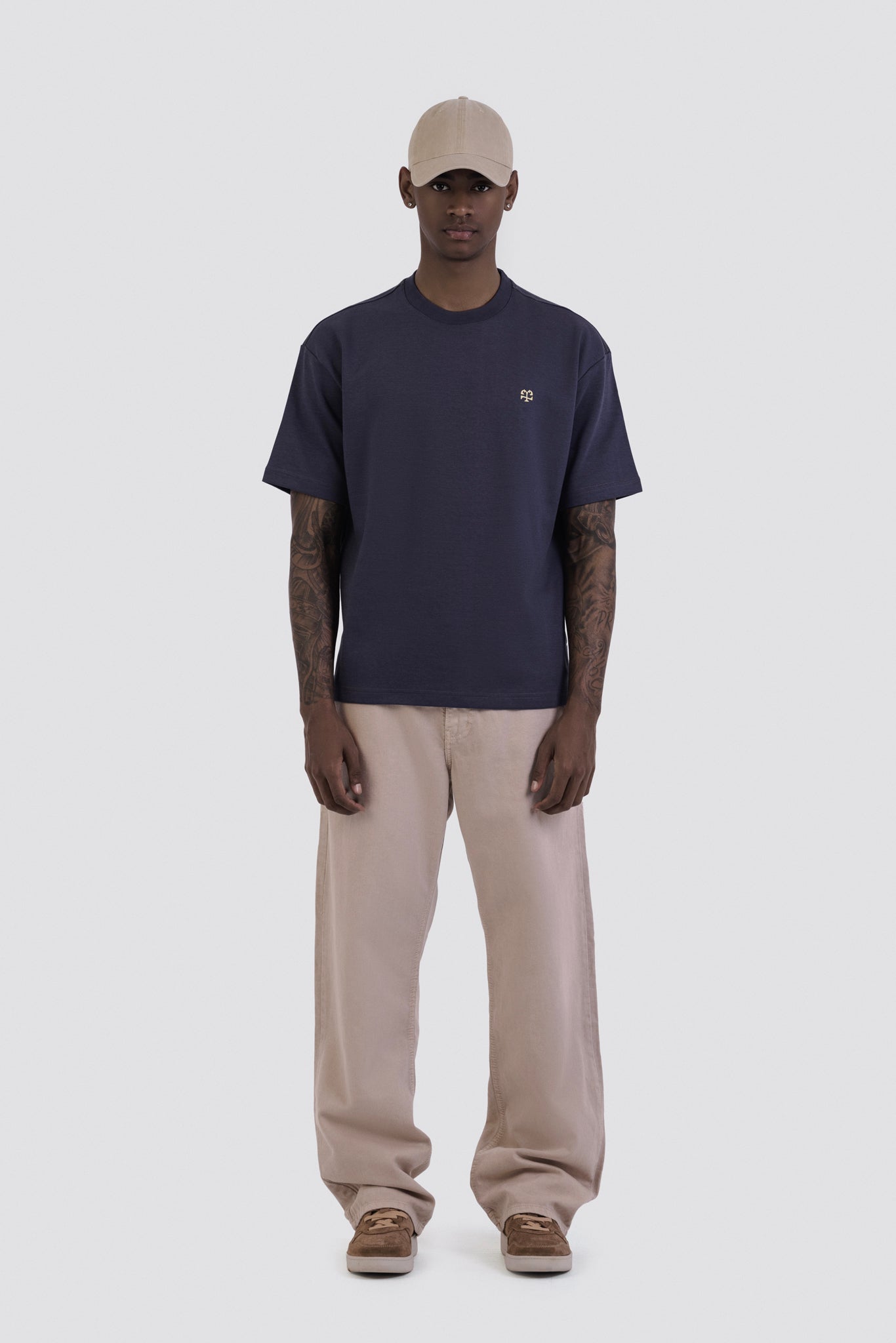 Person wearing a navy t-shirt, beige pants, and a cap on a white background