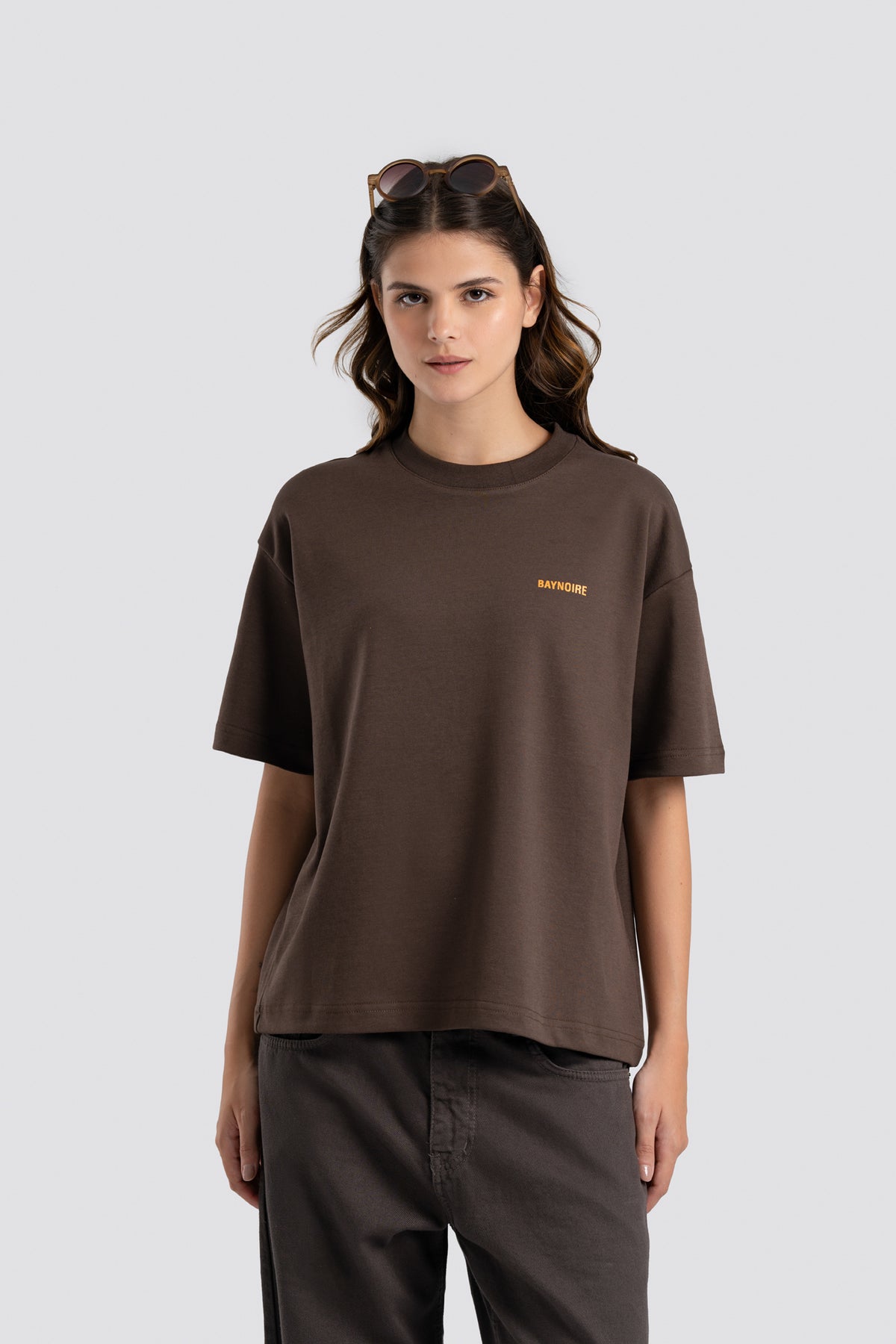 Woman wearing a brown t-shirt with a logo on a light gray background