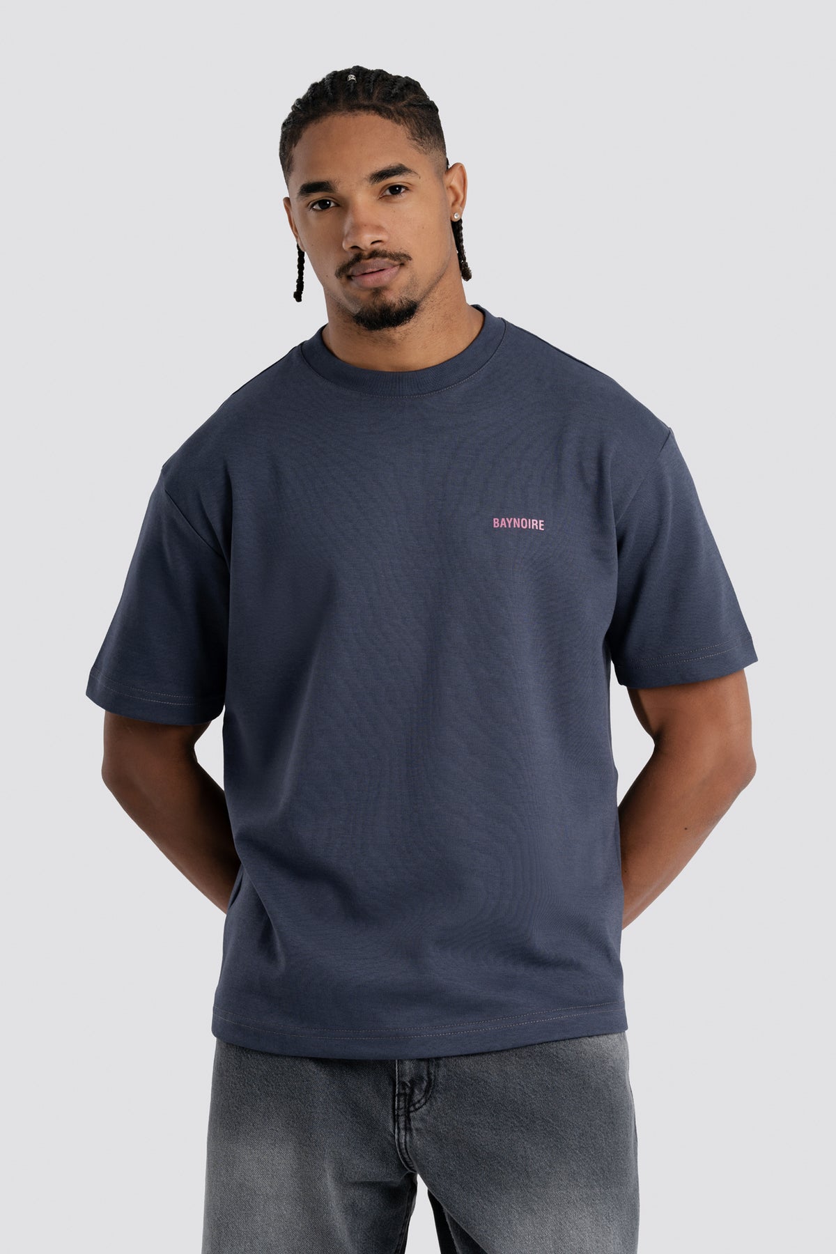 Man wearing a navy blue t-shirt with a small logo on a light gray background