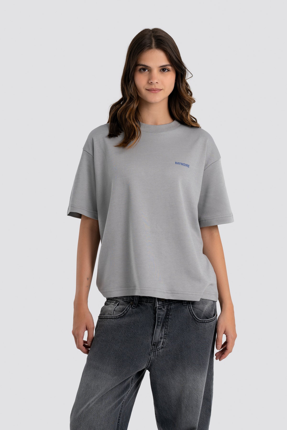 Woman wearing a gray t-shirt with a small logo on a light gray background