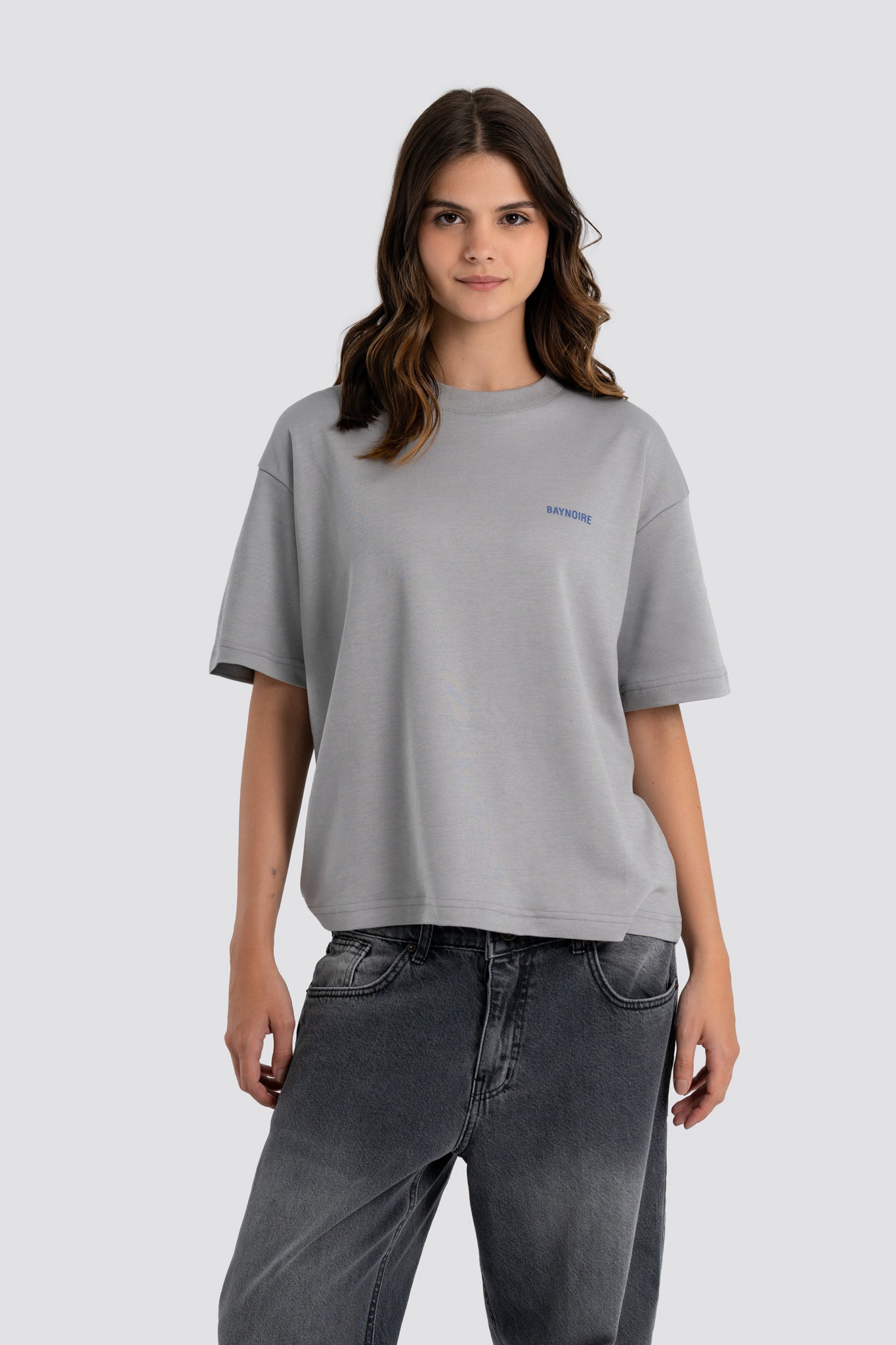 Woman wearing a gray t-shirt with a small logo on a light gray background
