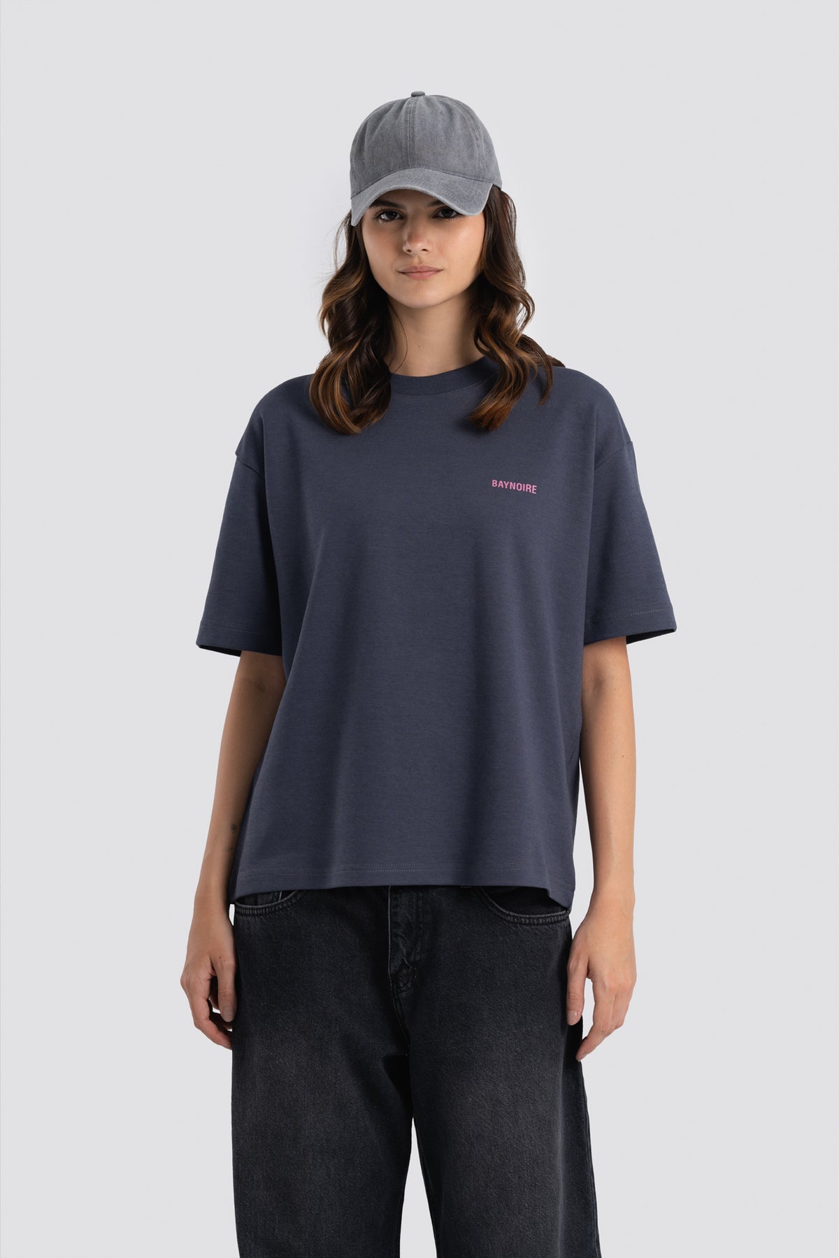 Person wearing a navy blue t-shirt with a small logo and a gray cap on a light gray background