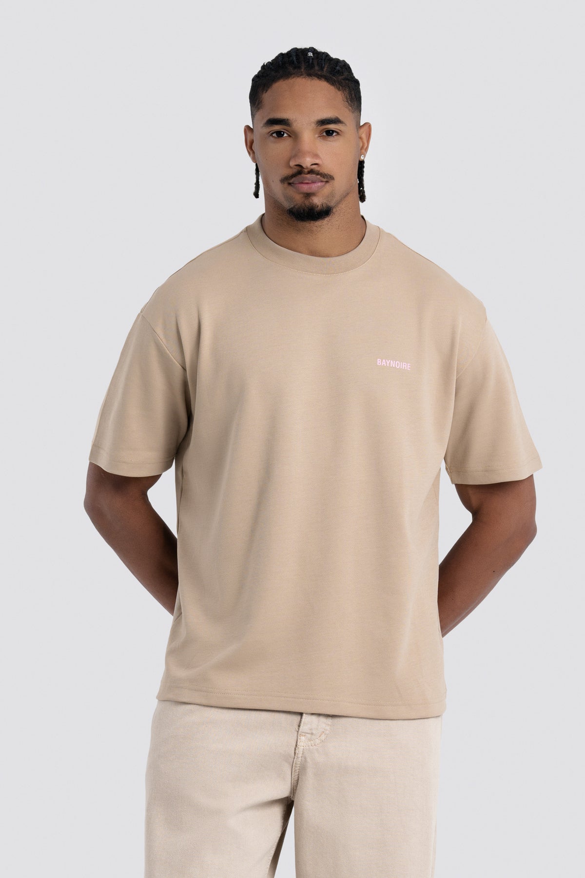 Man wearing a beige t-shirt with a small logo on a white background