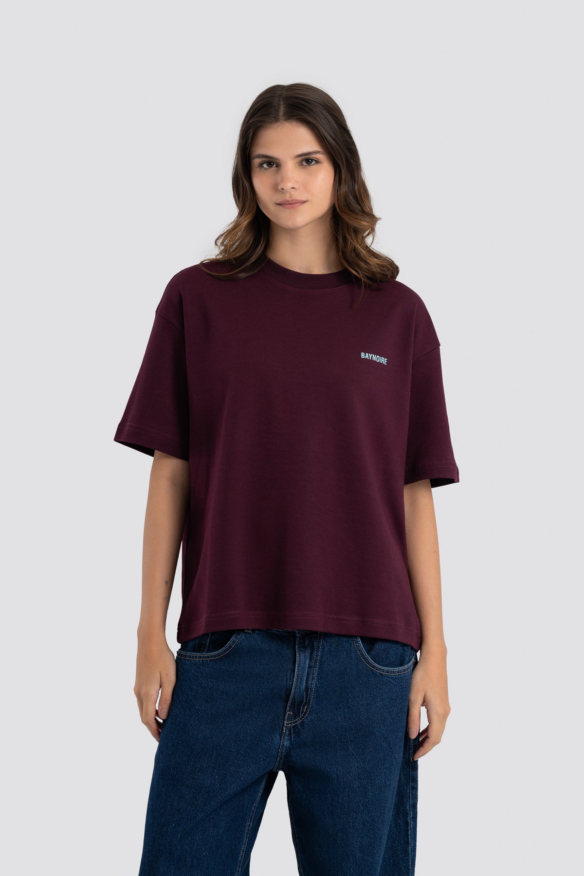 Person wearing a maroon t-shirt with a small white logo on a light gray background