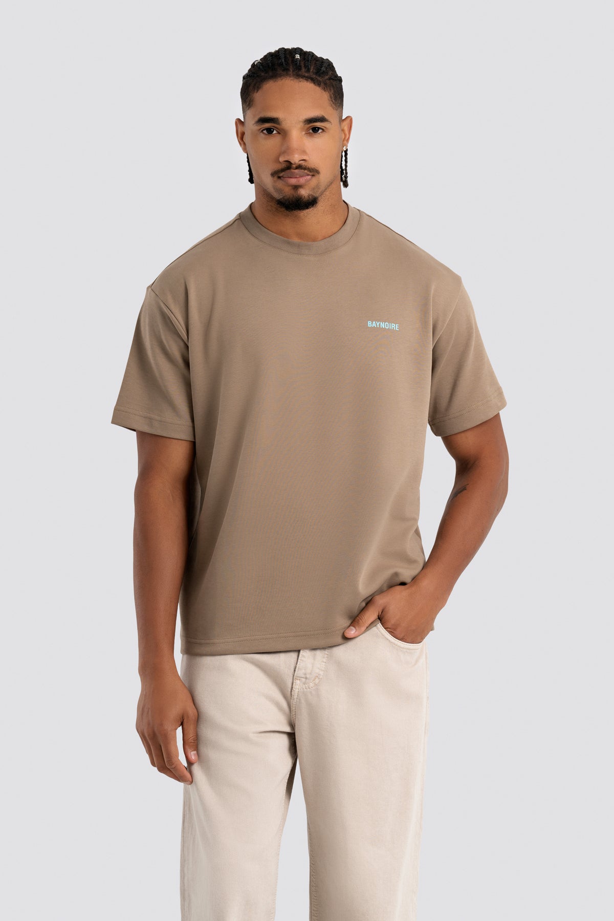 Man wearing a beige t-shirt with a small logo on a white background