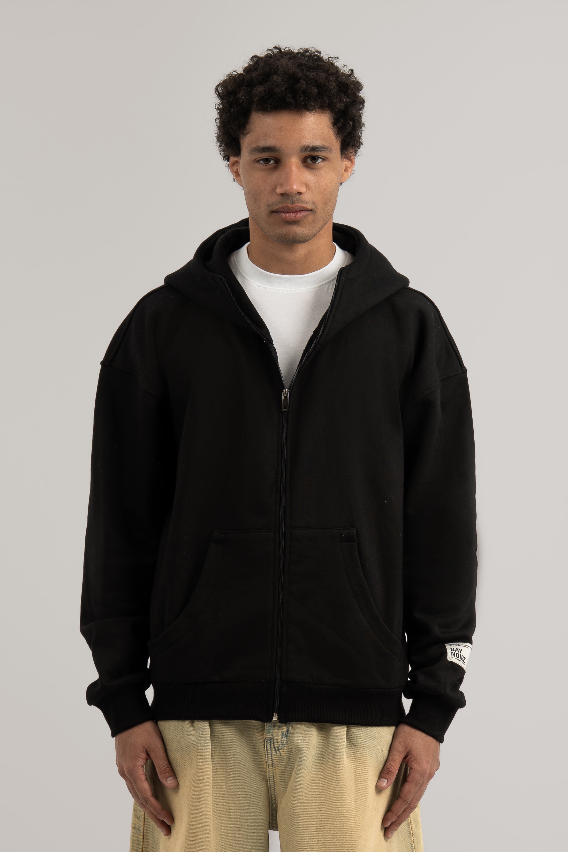 Person wearing a black hoodie with a white logo on a gray background